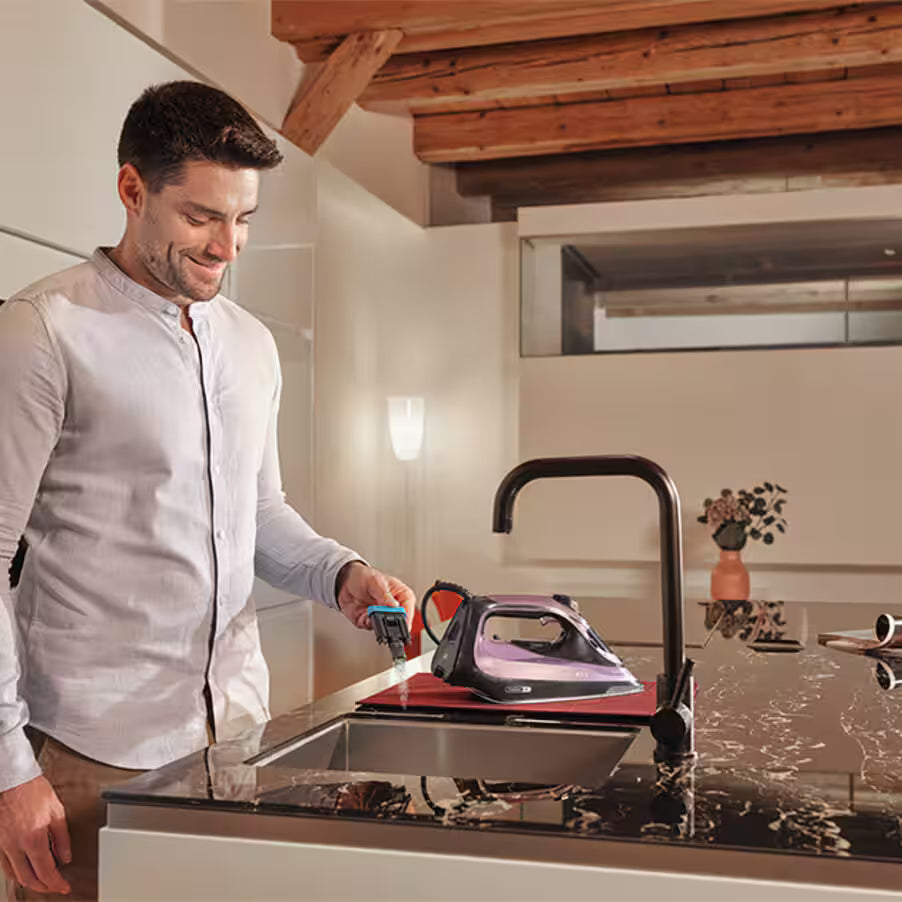 Man using a steam iron on a kitchen counter with wooden beams in the background