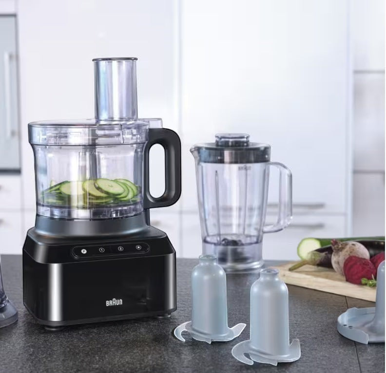 Braun PurEase food processor in black with sliced zucchini in the bowl and a blender attachment. Includes slicing disc and chopping blade.