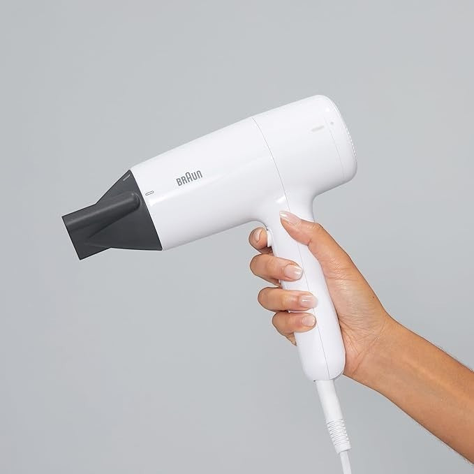 Taghareed Braun white 2100W hair dryer with ionic technology and concentrator nozzle, held by a hand.