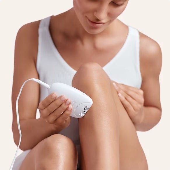 Taghareed Braun Silk-épil 1 epilator in white and pink, with 20 tweezers and SoftLift Tips, used on a woman's leg.
