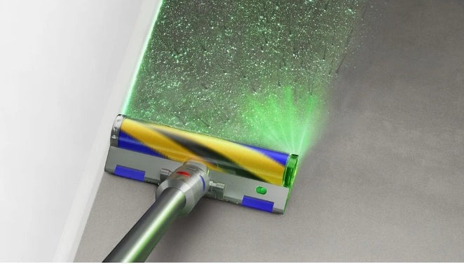 Taghareed cordless stick vacuum cleaner with illuminated floor head showing dust particles. Blue and yellow brush roll.