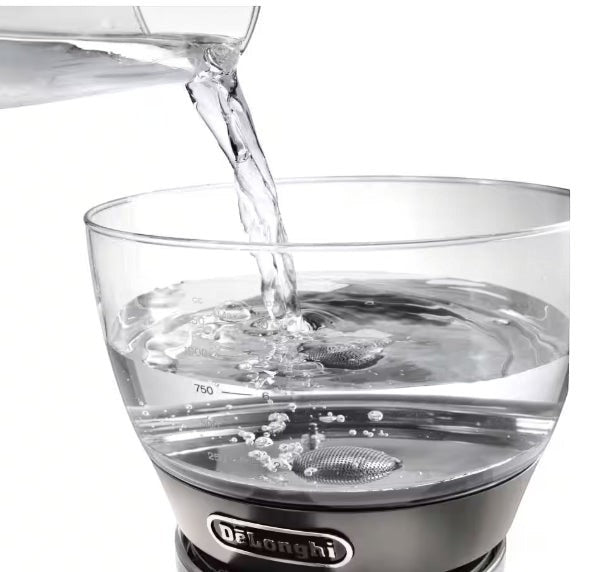 Taghareed De'Longhi Clessidra filter coffee maker, clear glass water tank with measurement markings, water being poured in.