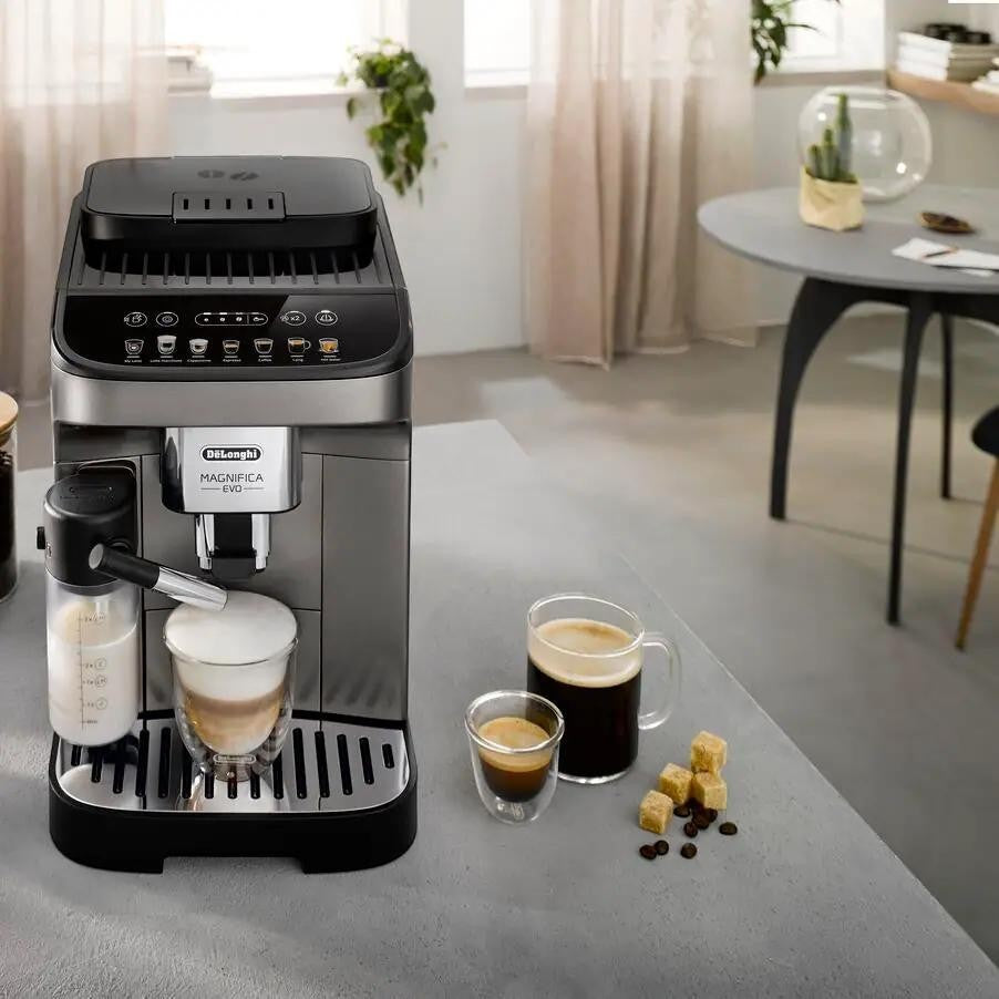 Taghareed De'Longhi Magnifica Evo automatic coffee machine in silver and black, with a milk carafe and two cups of coffee.