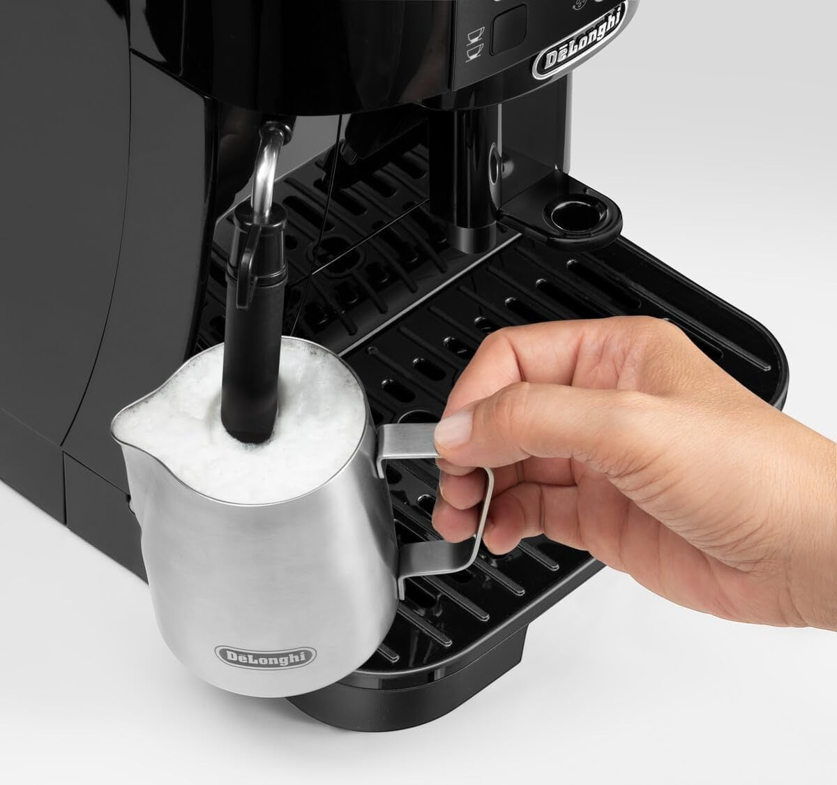 Taghareed De'Longhi Magnifica S black automatic coffee machine frothing milk with a stainless steel pitcher.