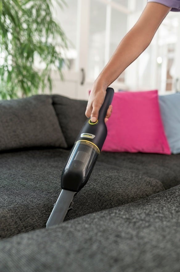 Taghareed Kärcher CVH 4 Black cordless hand vacuum cleaner with HEPA filter, used on a grey sofa.