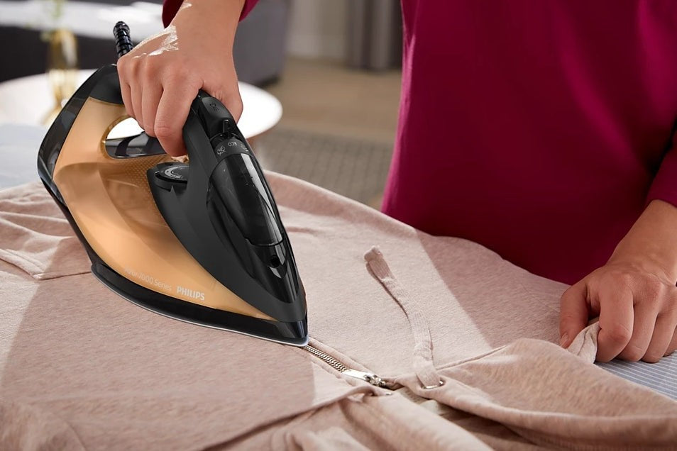 Taghareed Philips 7000 Series steam iron, black and gold, with SteamGlide Elite soleplate, used on a beige garment.