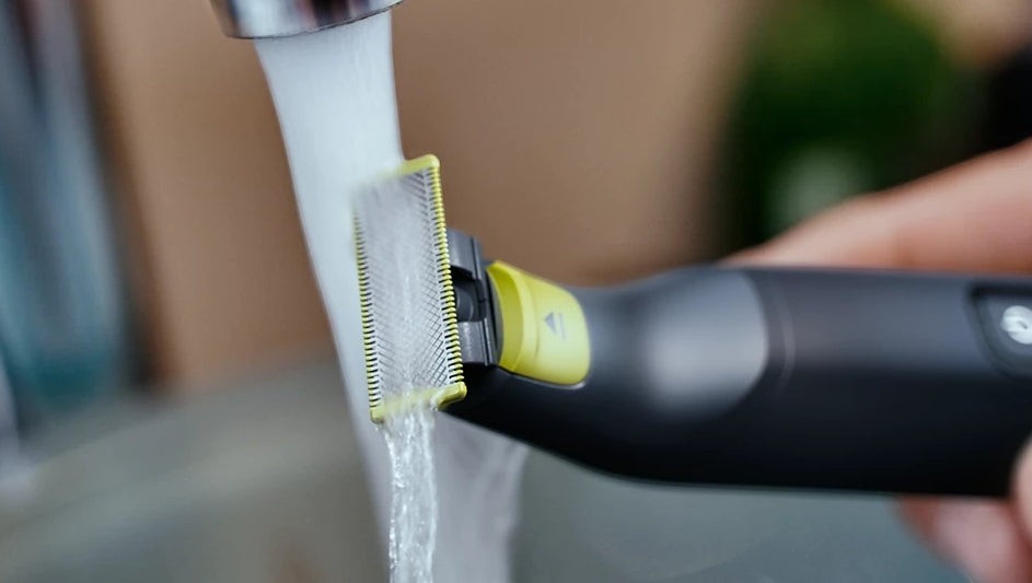Taghareed Philips OneBlade Pro QP6542/10 electric trimmer being rinsed under running water. Features a black body with a yellow accent.