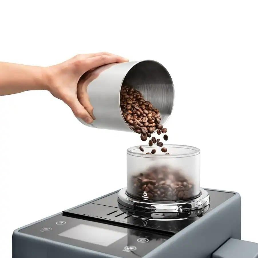 Taghareed Rivelia automatic coffee machine with dual bean hoppers, pouring coffee beans into the grinder.