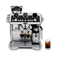 A De'Longhi espresso machine in polished stainless steel and black, shown with two espresso shots and an iced coffee glass on a white background.
