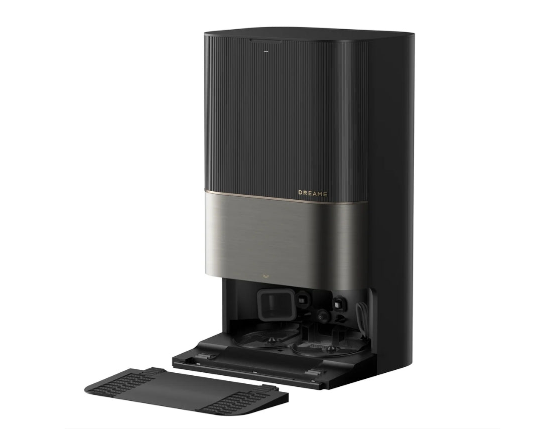 A Dreame automatic smart vacuum cleaner in a matte black finish with a brushed metallic silver middle band and a gold brand logo. The front cover is open, showing the base and a black floor mat on a clean white background.