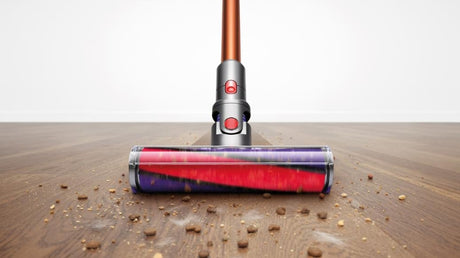 Cordless vacuum cleaner on a wooden floor with dirt particles.