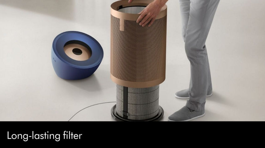 A person is shown replacing a cylindrical air filter on a floor-standing device, with a blue circular component placed beside it on a light studio floor. Text at the bottom reads 'Long-lasting filter'.