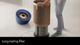A person is shown replacing a cylindrical air filter on a floor-standing device, with a blue circular component placed beside it on a light studio floor. Text at the bottom reads 'Long-lasting filter'.