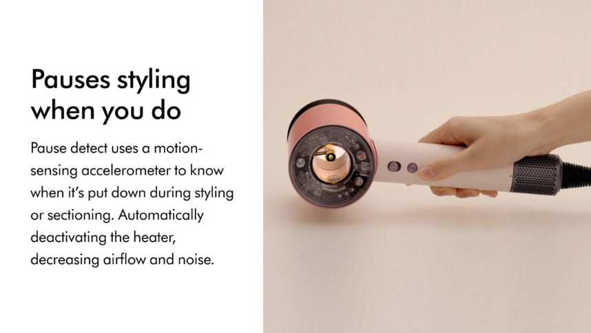 A hand holds a pink and white hair dryer against a warm beige background, with text on the left explaining that the dryer pauses styling when detected.