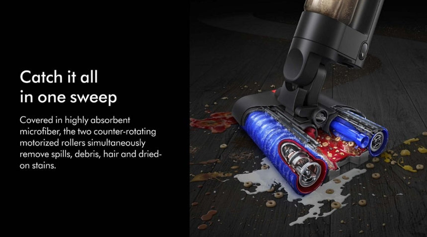 A close-up promotional shot of a cordless vacuum cleaner head on a dark wooden floor, showing blue and red motorized roller brushes catching spilled liquid and debris. Text on the left reads, 'Catch it all in one sweep' with additional product feature copy.