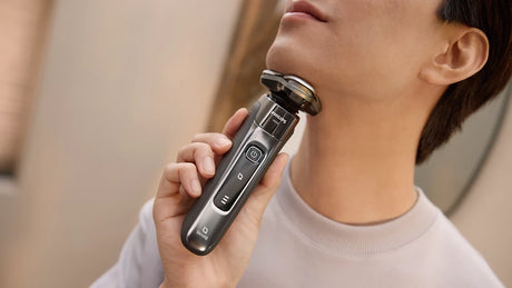 Person using a electric shaver on their neck with a neutral background