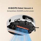 Xiaomi Robot Vacuum 6 shown from an elevated angle with its underside open to reveal the cleaning brush bar and suction channels. Blue airflow lines illustrate suction power, set against a light beige background with text reading 'XIAOMI Robot Vacuum 6' and 'Extraordinary 30,000Pa suction power'.