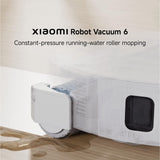 Xiaomi Robot Vacuum 6 shown mopping a wooden floor with a puddle of water, under the text 'Xiaomi Robot Vacuum 6 Constant-pressure running-water roller mopping'.