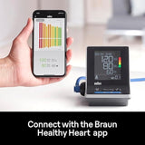 Braun upper arm blood pressure monitor with Bluetooth connectivity, shown with a smartphone displaying the Braun Healthy Heart app.