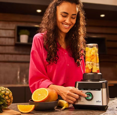 Braun PowerBlend 7 blender with a woman making a fruit smoothie. Silver and black appliance with a clear jug filled with fruit.