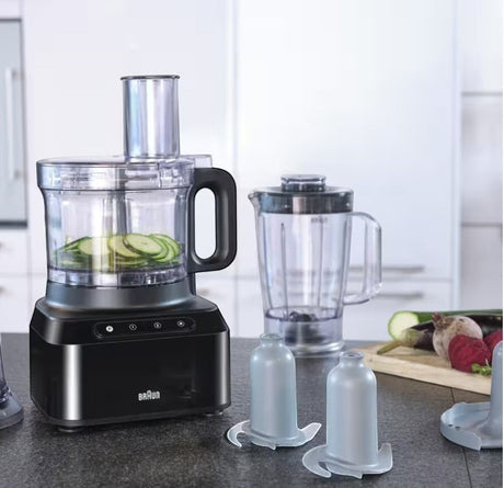 Braun PurEase food processor in black with sliced zucchini in the bowl and a blender attachment. Includes slicing disc and chopping blade.