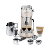 A De'Longhi espresso machine in champagne gold with stainless steel accessories, shown on a clean white background. The set includes two espresso cups filled with espresso, a milk pitcher, an espresso portafilter, a tamper, two metal filter baskets, and a double-walled glass cup with a layered latte.