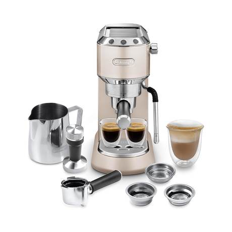 A De'Longhi espresso machine in champagne gold with stainless steel accessories, shown on a clean white background. The set includes two espresso cups filled with espresso, a milk pitcher, an espresso portafilter, a tamper, two metal filter baskets, and a double-walled glass cup with a layered latte.