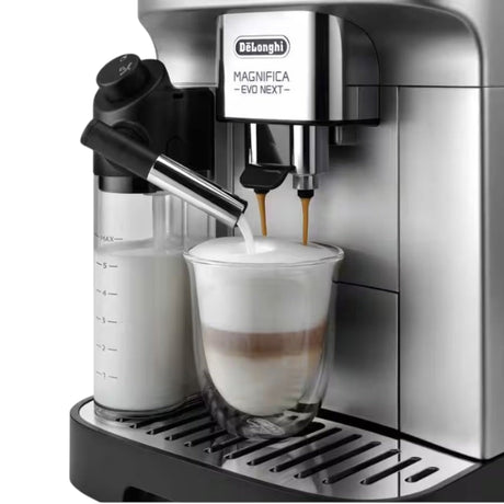 De'Longhi Magnifica Evo coffee machine making a latte with frothed milk and espresso in a glass cup.