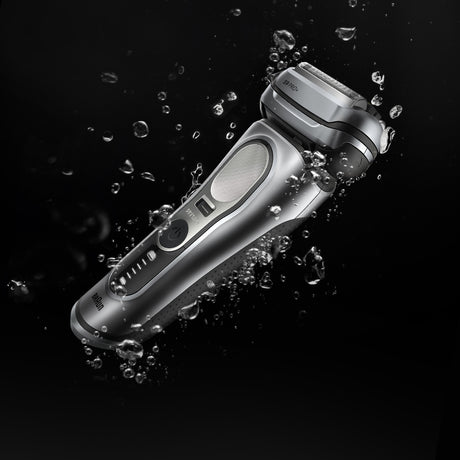 Silver electric shaver with water droplets on a black background
