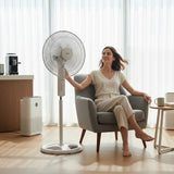 Tagahareed Sona 18" white stand fan with adjustable height and oscillating head, cooling a woman relaxing in a chair.