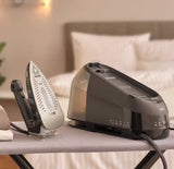Taghareed Braun CareStyle 5 IS5249BK steam generator iron with 2L water tank and ergonomic handle, on ironing board.