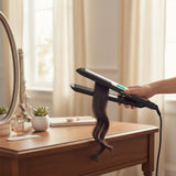 Taghareed Braun Satin Hair 7 IONTEC hair straightener with black ceramic plates, styling dark hair with a wavy effect.