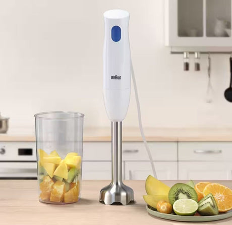 Taghareed Braun MultiQuick 1 hand blender, white with blue button, stainless steel shaft, with fruit in beaker and on plate.