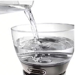 Taghareed De'Longhi Clessidra filter coffee maker, clear glass water tank with measurement markings, water being poured in.