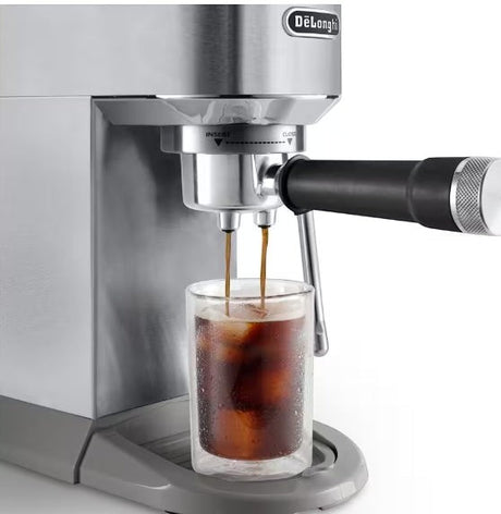 Taghareed De'Longhi Dedica Duo stainless steel espresso machine brewing cold brew coffee into a glass with ice.