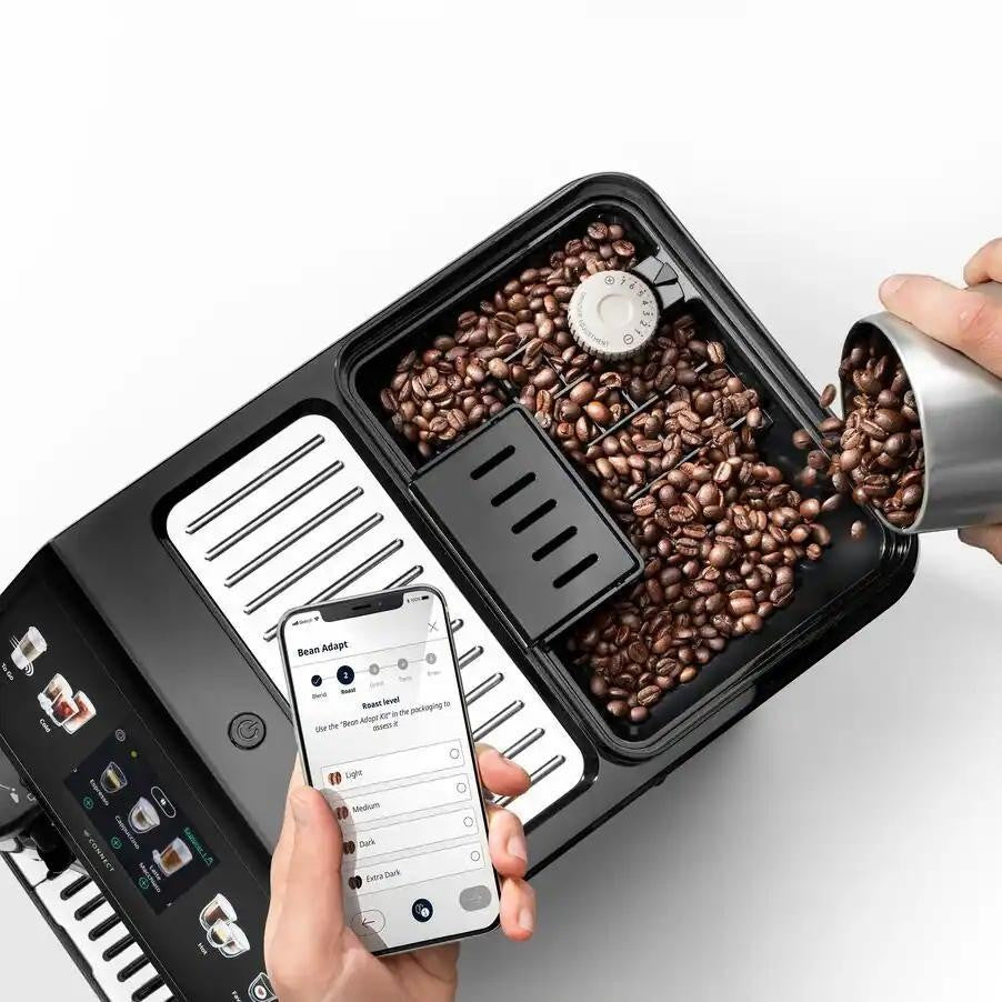 Taghareed De'Longhi Eletta Explore coffee machine with bean hopper and smartphone app interface showing Bean Adapt settings.