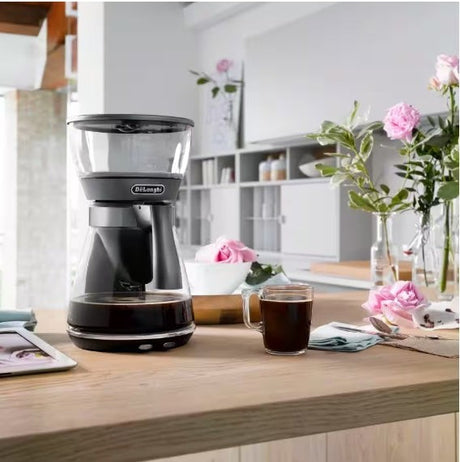 Taghareed De'Longhi ICM17210 black glass and metal filter coffee maker with 1.25L carafe and pour-over mode.