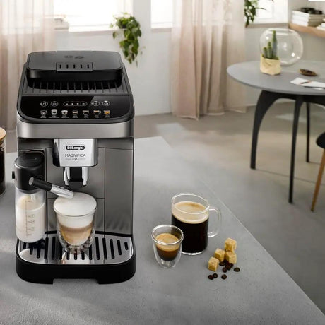 Taghareed De'Longhi Magnifica Evo automatic coffee machine in silver and black, with a milk carafe and two cups of coffee.