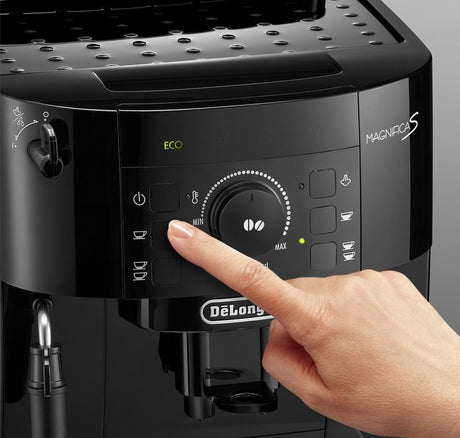 Taghareed De'Longhi Magnifica S black automatic coffee machine with a finger pressing a button.