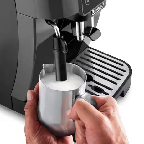 Taghareed De’Longhi Magnifica Start coffee machine frothing milk in a stainless steel pitcher. Black automatic espresso maker.