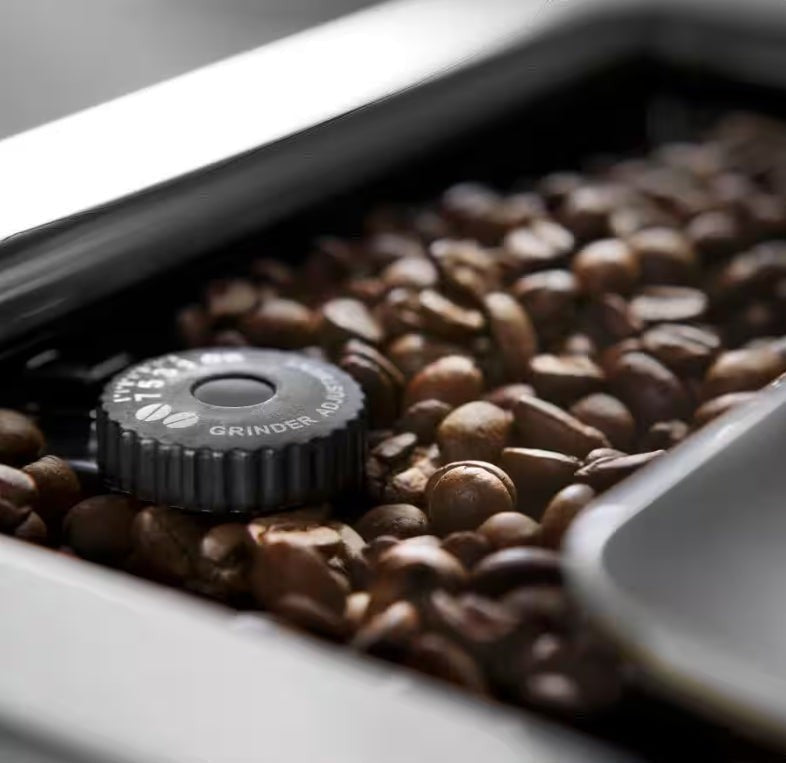 Taghareed De’Longhi PrimaDonna Elite coffee machine grinder adjustment dial surrounded by coffee beans.