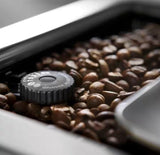 Taghareed De’Longhi PrimaDonna Elite coffee machine grinder adjustment dial surrounded by coffee beans.