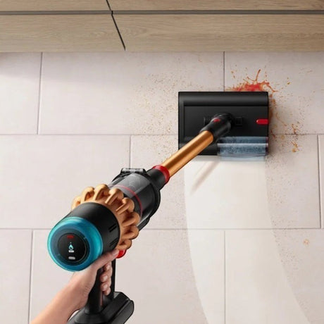 Taghareed Dyson V16 Piston Animal Submarine cordless vacuum in copper and black, cleaning spills on a tiled wall.