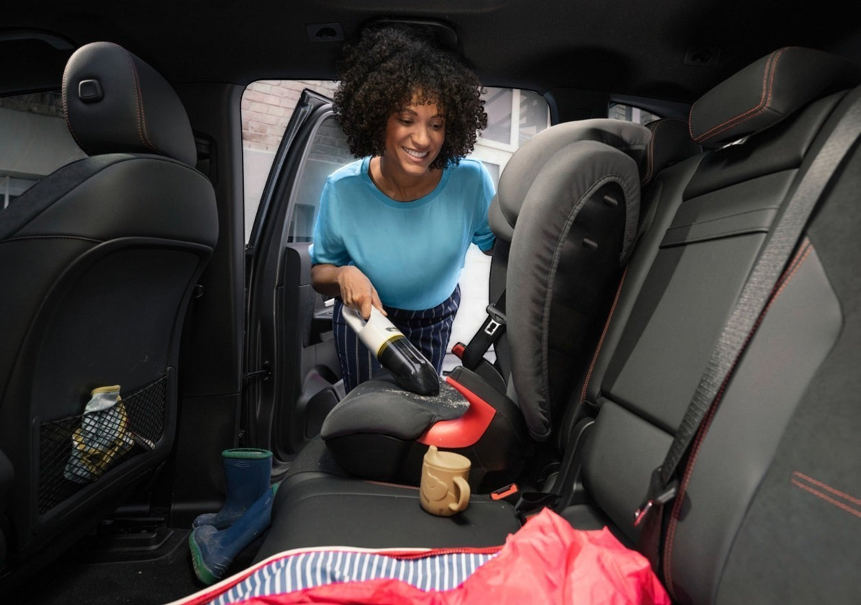 Taghareed Kärcher CVH 2 cordless hand vacuum cleaner with HEPA filter, used by a woman to clean a car seat.