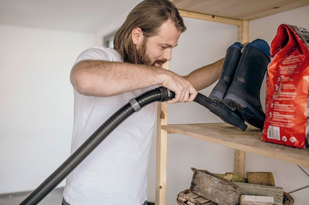 Taghareed Kärcher WD 3 S V wet & dry vacuum cleaner with 17L stainless steel container, used by a man to clean boots on a shelf.