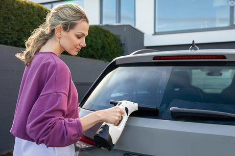 Taghareed Kärcher Window Vac WV 2 Plus cordless window cleaner in white and black, used by a woman on a car window.