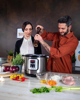 Taghareed: Kenwood 8L 16-in-1 electric pressure cooker in silver and black, with digital display, being used by a couple preparing ingredients.