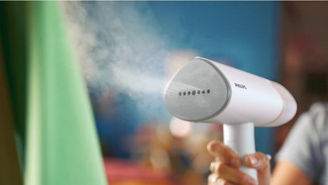 Taghareed Philips 3000 Series handheld garment steamer, white and grey, with steam emitting from the nozzle.