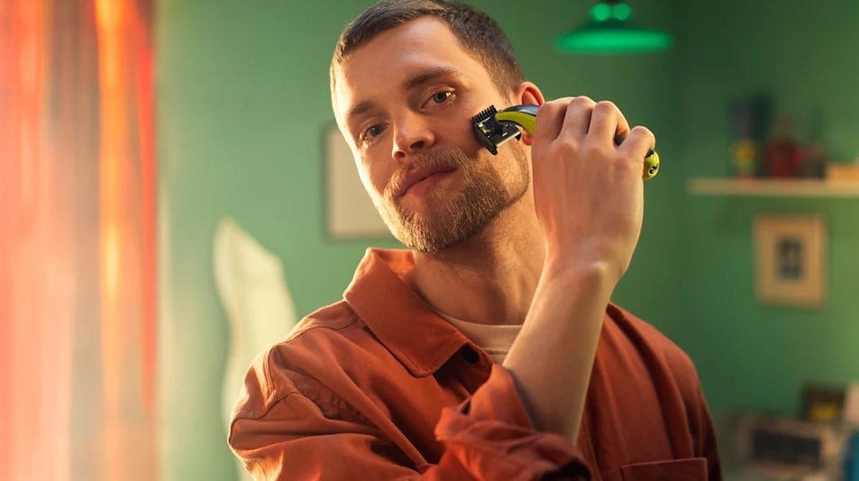 Taghareed Philips OneBlade QP2824/10 electric trimmer with yellow and black accents, used by a man on his face.