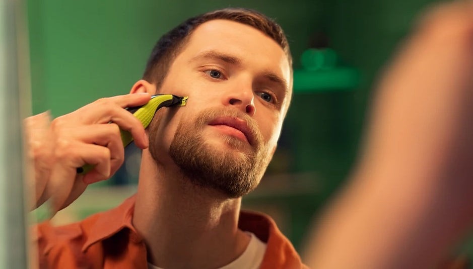 Taghareed Philips OneBlade QP2824/10 electric trimmer with green accents, used by a man to trim his beard.